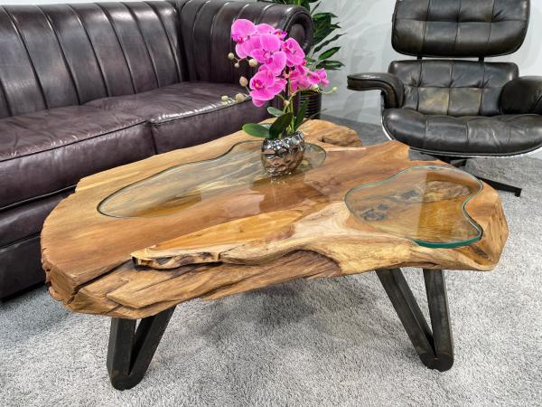 Baumstamm-Couchtisch mit Glasplatte und schwarzen Beinen.
