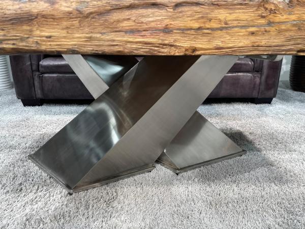 Wohnzimmertisch mit gekreuztem Edelstahlgestell und Holzplatte.