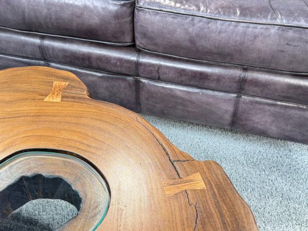 Wohnzimmertisch aus Suar-Holz mit Glasmitte, vor Ledersofa.