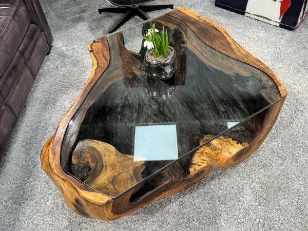 Runder Wohnzimmertisch aus Suar-Baumstamm auf grauem Teppich.