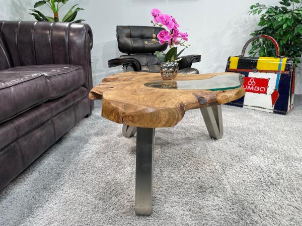 Tree trunk coffee table with glass top and metal legs in living room.
